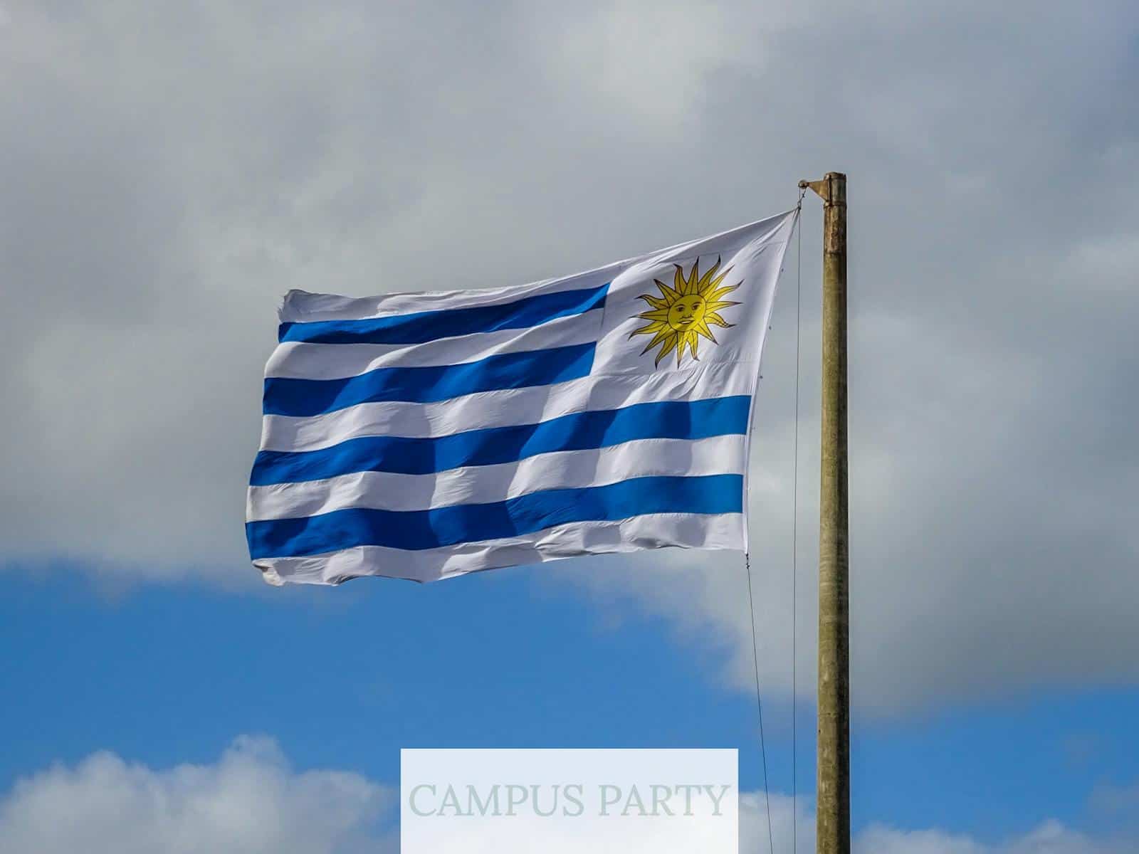 The national flag of Uruguay waves on a flagpole against a bright cloudy sky in Punta del Este.